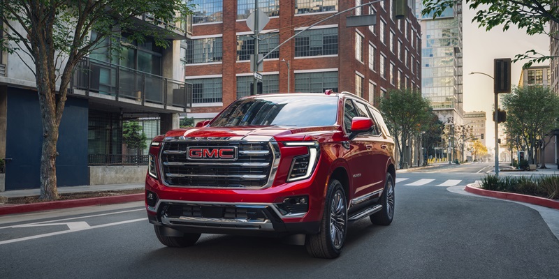 Red 2026 GMC Yukon driving through the business district of a city